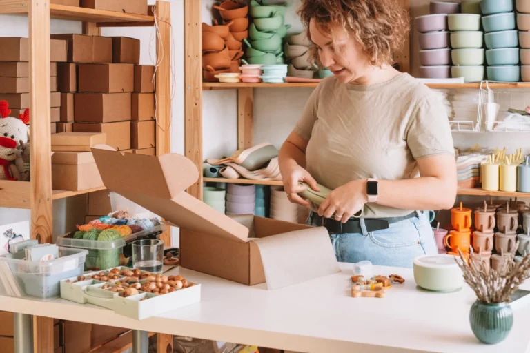 smiling concentrated curly woman packing wrapping shipment with silicone baby dish box delivery work home